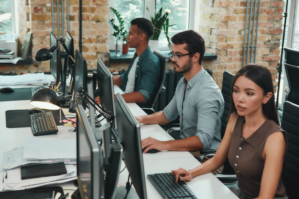 Group of young IT employees working on computers while sitting in a modern open space.