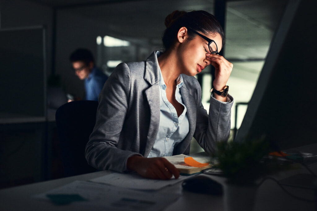 Stressed business woman working late on a computer in an office, struggling with reducing administrative burdens.